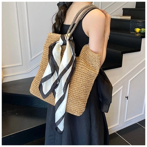 Detail shot of a large straw tote bag with black and white braided handle and scarf