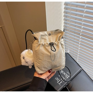 Beige lightweight nylon drawstring crossbody bag with cute plush pom-pom charm and black strap