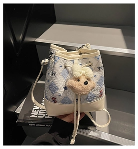 Detail of drawstring bucket bag with quilted pattern, teddy bear charm and bow decoration