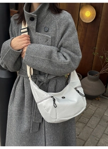 Detail of white crescent crossbody bag with woven zipper pulls and wide fabric strap