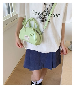 Détail du sac Boston vert clair porté à l'épaule avec une bandoulière réglable