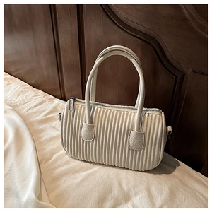 Detail view of cream white pleated hobo bag with quilted ripples on soft white bedding