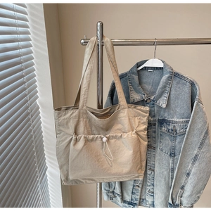 Detail of beige large capacity tote bag with drawstring pocket on a hanging display