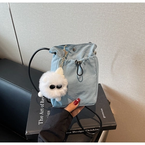 Detail of light blue nylon drawstring bucket bag with white faux fur pompom charm