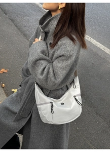 Close-up of a white crescent crossbody bag with detailed knotted zipper on asphalt background