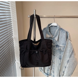 Macro shot of a black tote bag featuring a functional drawstring front pocket and long strap