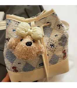 Detail of beige bucket bag with embossed pattern, plaid bear design and plush dog charm