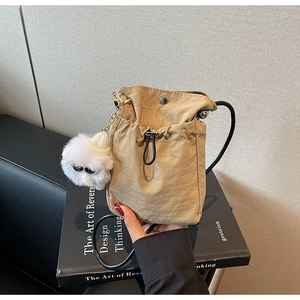 Detailed shot of khaki nylon bucket bag with a white plush sheep charm on a book