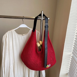 Detail of red knit tote bag featuring black leather strap and colorful flower charm