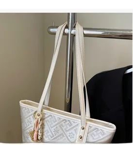 Detail of cream tote bag with geometric patterns, long handles, and gold rivet accents