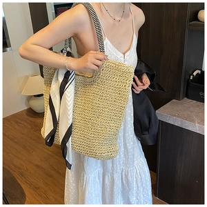 Close-up of woven straw tote bag with black and white striped straps and silk scarf