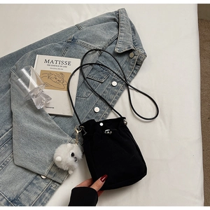 Detail of a black bucket bag with a plush white charm and elegant leather shoulder strap