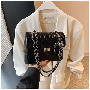 Detail of black quilted shoulder bag with silver chain and sphere pendant in hand