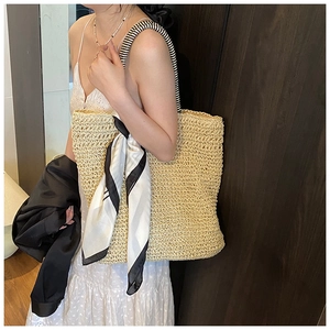 Detail of woven straw tote bag with black and white striped handles and silk scarf