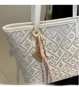 Close-up of white tote bag with geometric patterns, gold ring handle, and abacus charm detail