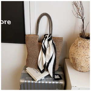 Detail of hand-woven straw tote bag with black and white scarf tied on silver suitcase
