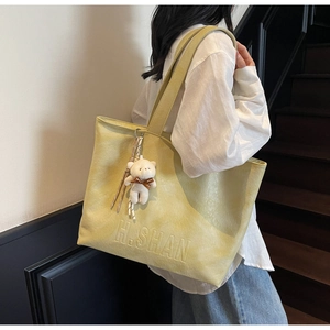 Detail of mustard tote bag featuring embossed logo, plush bear charm, and striped silk scarf