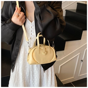 Close-up of cream heart-shaped mini handbag featuring dual handles and a leather strap