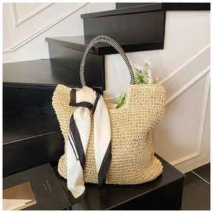 Detail of hand-woven straw tote bag with striped handle and silk scarf on black stairs