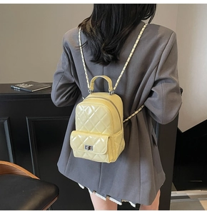 Detail of a pale yellow quilted patent leather mini backpack with chain straps and metal clasp