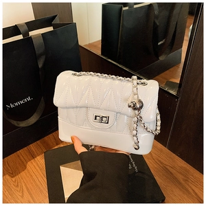 Close-up of white quilted crossbody bag with silver chain strap and metal ball detail