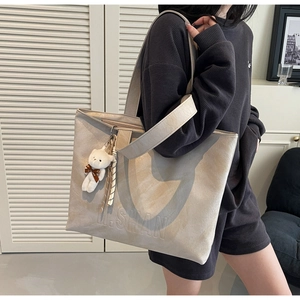 Detail of large beige tote bag featuring H.SHAN logo and cute plush bear accessory