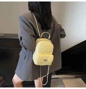Detail view of bright yellow quilted mini backpack with silver metal chain on a model