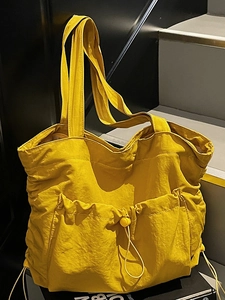 Large bright yellow nylon tote bag with drawstring pockets on grey stairs