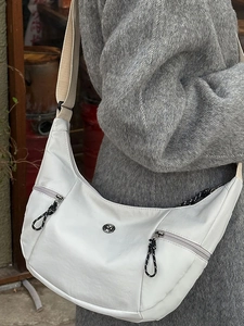 White crescent crossbody bag with dual front zippers and wide fabric strap worn by a model