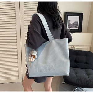 Detail of light blue suede tote bag with H.SHAN logo and cute white teddy bear charm