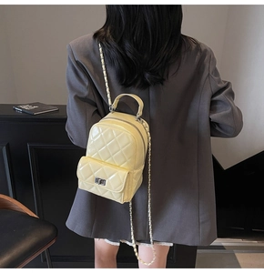Pale yellow quilted leather backpack with gold clasp on a model in a modern interior