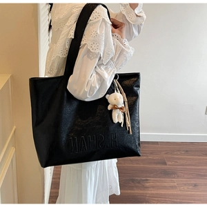 Detail of black faux leather tote bag featuring brand embossing and a cute bear charm