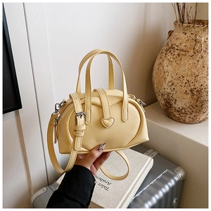 Close-up of a pale yellow heart-accented handbag on books and silver suitcase