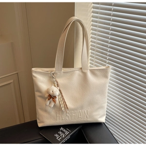 Detail of off-white leather tote bag with H.SHAN embossing and plush bear charm
