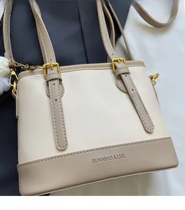 Close-up of beige bucket bag with gold hardware and a fluffy white pompom charm