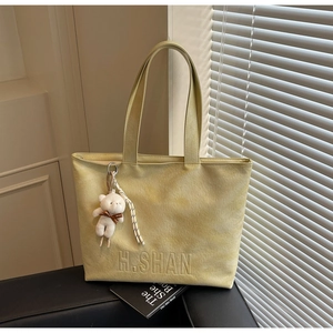 Close-up of light green tote bag with embossed H.SHAN logo and white plush bear charm