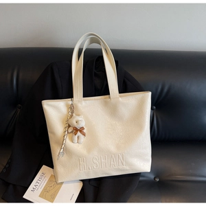 Detail of cream leather tote bag with H.SHAN logo, bear charm and silk scarf decoration