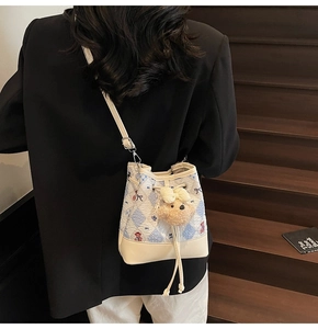 Detail of blue and white checkered bucket bag with leather base and plush bear charm