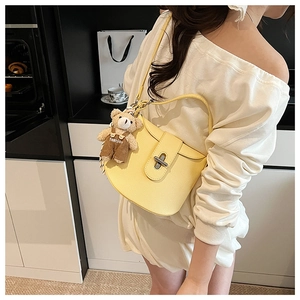 Detail view of yellow leather saddle bag with silver twist lock and cute bear charm