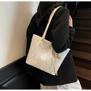 Detail of white tote bag featuring geometric patterns, silk scarf, and gold charm
