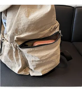 Detail of front zipper pocket on beige nylon backpack showing storage space for a long wallet