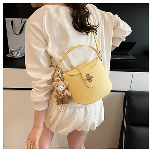 Detail view of yellow lychee grain leather handbag with metal twist lock and bear charm