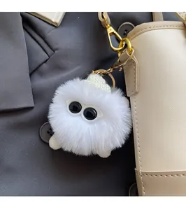 Close-up of a white plush monster charm with big eyes on a beige leather bucket bag