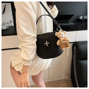 Detail of black litchi leather saddle bag featuring a silver cross lock and bear charm