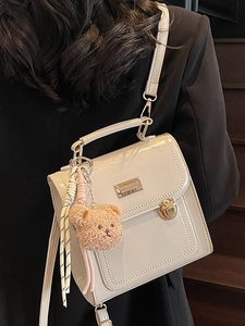 Borsa a mano strutturata in pelle crema con fibbia dorata e ciondolo a orso su modella