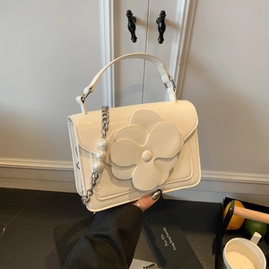 Detailed view of the 3D camellia flower and pearl charm on a white PU leather handbag