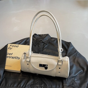 Détail d'un sac cylindrique blanc crème avec pendentif coeur sur fond en cuir noir