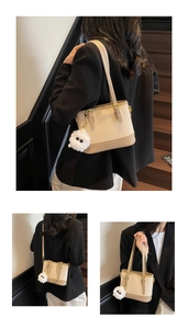 Detail showing creamy bucket bag with brown trim and plush charm on wooden stairs
