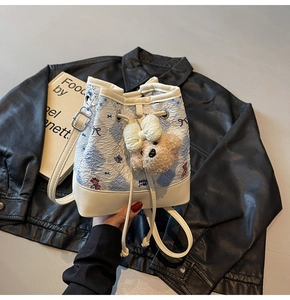 Detail of blue plaid bucket bag featuring bear embroidery and plush charm accessory