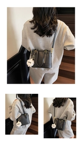 Detail of black textured bucket bag with plush white doll charm and shoulder strap